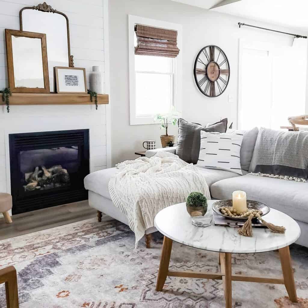 A white marble coffee table with wooden legs and a gray couch are arranged in front of a white shiplap fireplace.