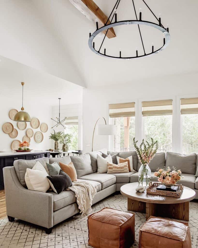 Black wagon wheel chandelier hangs from a vaulted ceiling over a stained wood round coffee table with a sectional sofa.