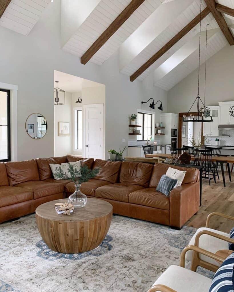 wood round coffee table next to brown leather couch in living room with vaulted ceilings