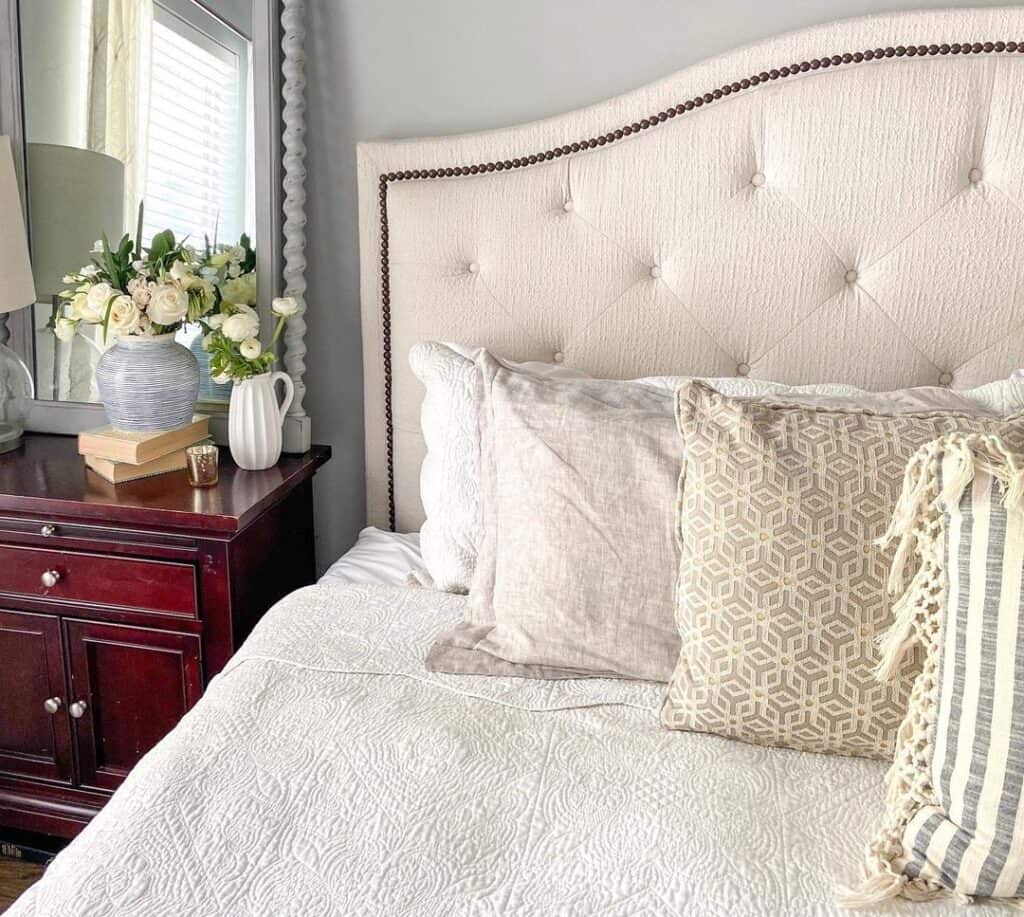 White Flowers Next to a White Tufted Upholstered Bed